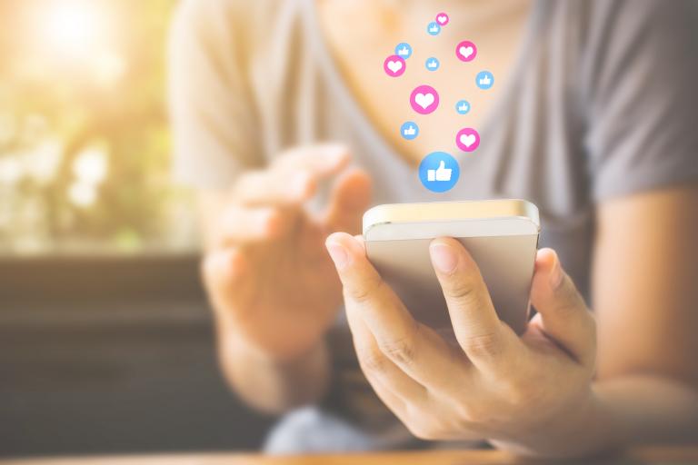 Frau mit Handy in der Hand, Herz- und Daumen hoch Icons über dem Handy